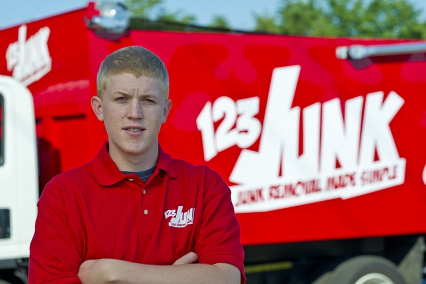 A staff in a red 123JUNK polo shirt standing with arms crossed in front of a red company truck