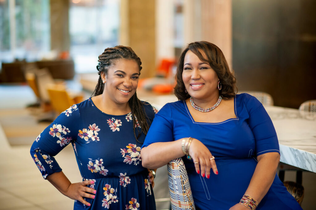 Two women in blue dresses smiling and posing indoors