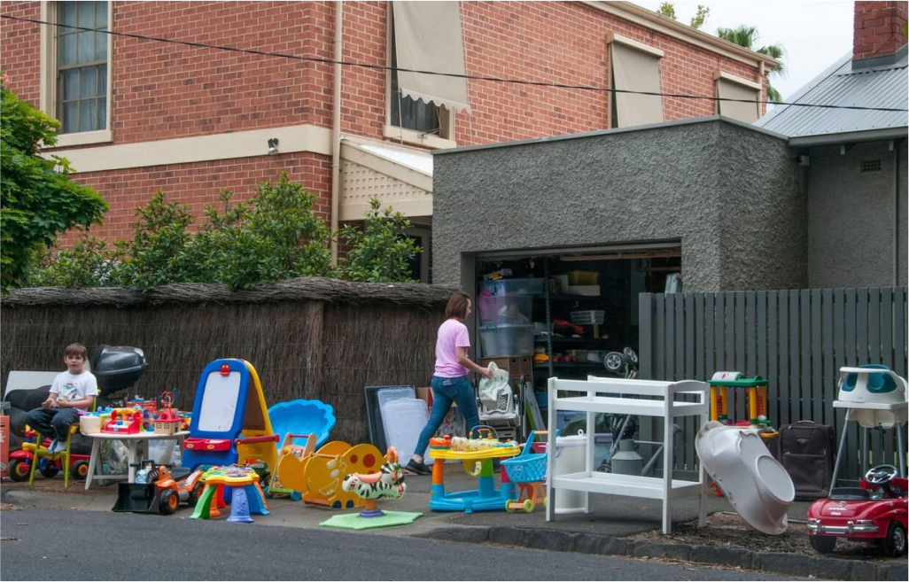 Outdoor scene with children’s toys and play equipment arranged for sale in front of a house garage