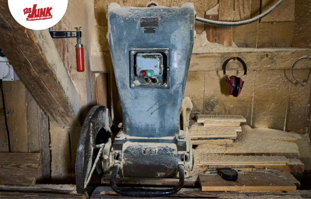 Old industrial woodworking machine covered in sawdust, surrounded by wooden planks and tools